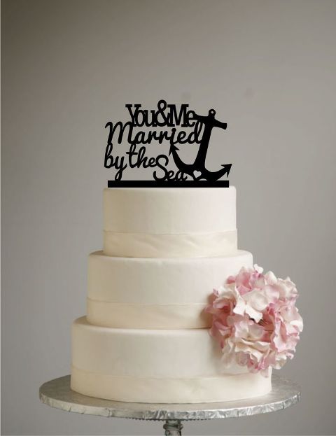 a white buttercream wedding cake decorated with pink blooms, a black calligraphy topper and an anchor is a lovely solution for a nautical wedding