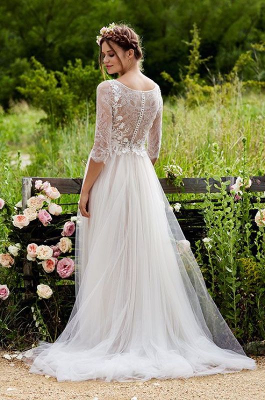 a refined boho spring bridal look with an A-line wedding dress with a lace bodice and a tulle skirt with long sleeves plus blooms tucked in the hair