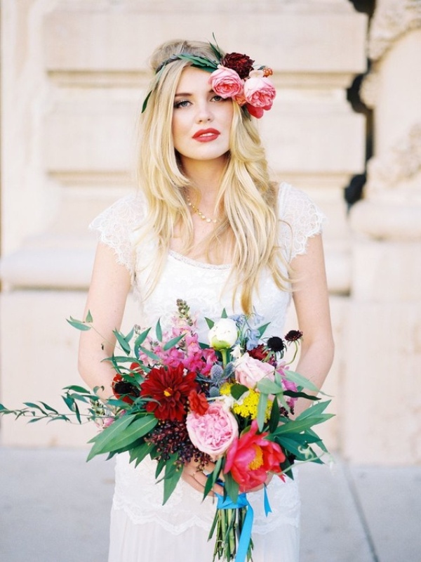 a boho bridal look with a lace wedding dress with cap sleeves, a bright floral crown and a bold wedding bouquet