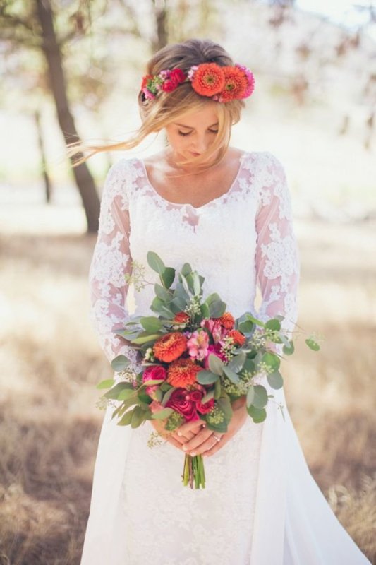 a boho bridal look with a romantic lace long sleeve wedding dress, a pink and orange flower crown and a bouquet with greenery is a great idea