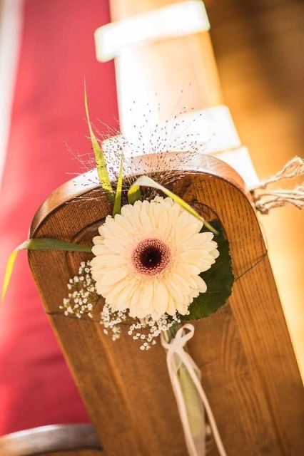a delicate aisle bench decoration of a white gerbera and some greenery is a lovely idea for a rustic or just laid-back wedding