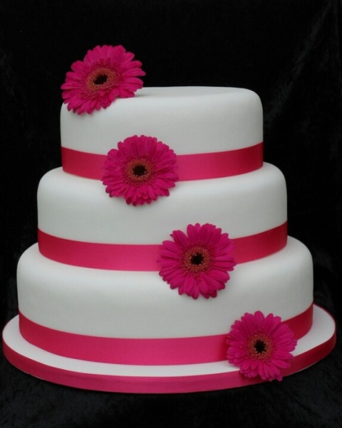 a round wedding cake with pink ribbon and pink gerberas is a cool and bold idea for a spring or summer wedding
