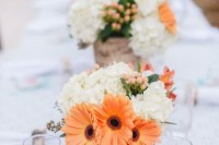 a contrasting wedding centerpiece of white hydrangeas, berries and orange gerberas and greenery is a bold and cool idea for spring or summer