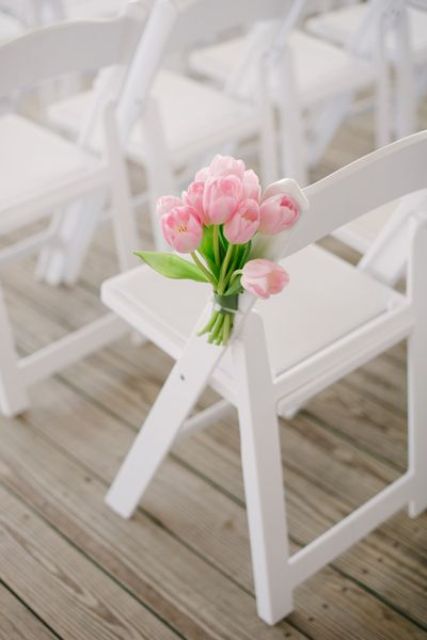 white aisle chairs decorated with delicate pink tulips look very nice and chic and make your wedding ceremony space cooler