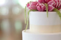 a white wedding cake topped with pink tulips and greenery is a lovely idea for a modern wedding, it will add color and interest to the dessert table