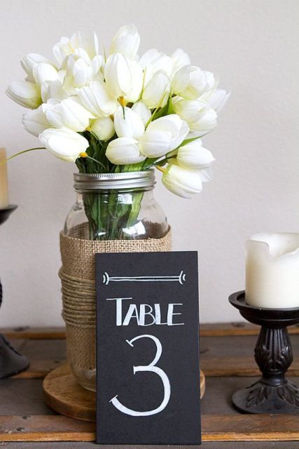 an elegant wedding centerpiece of a jar with white tulips and butlap and a chalkboard table number for a rustic wedding