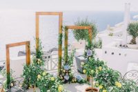 a Greek wedding ceremony space with large frames, with greenery and pastel blooms, lemon trees in pots that line up the aisle