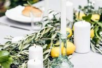 a Tuscan wedding tablescape with a lush greenery table runner and lemons, pillar and tall and thin candles is awesome