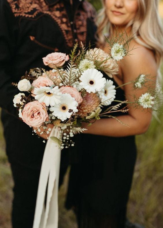 a beautiful and delicate wedding bouquet of white gerberas, blush blooms and some baby's breath, greenery and ribbon