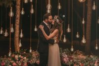a beautiful and romantic wedding ceremony space with lots of bulbs hanging down and lush pink florals and greenery aorund