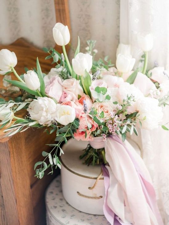 a beautiful pastel wedding bouquet of white tulips, blush and peachy roses and greenery and waxflower plus ribbons is a dreamy and fresh idea