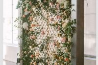 a beautiful wedding backdrop of greenery, pink, peachy and white blooms, foliage on the floor for indoors