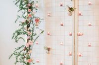 a beautiful wedding backdrop with greenery, pink blooms and pink candleholders attached all over the backdrop is a lovely idea