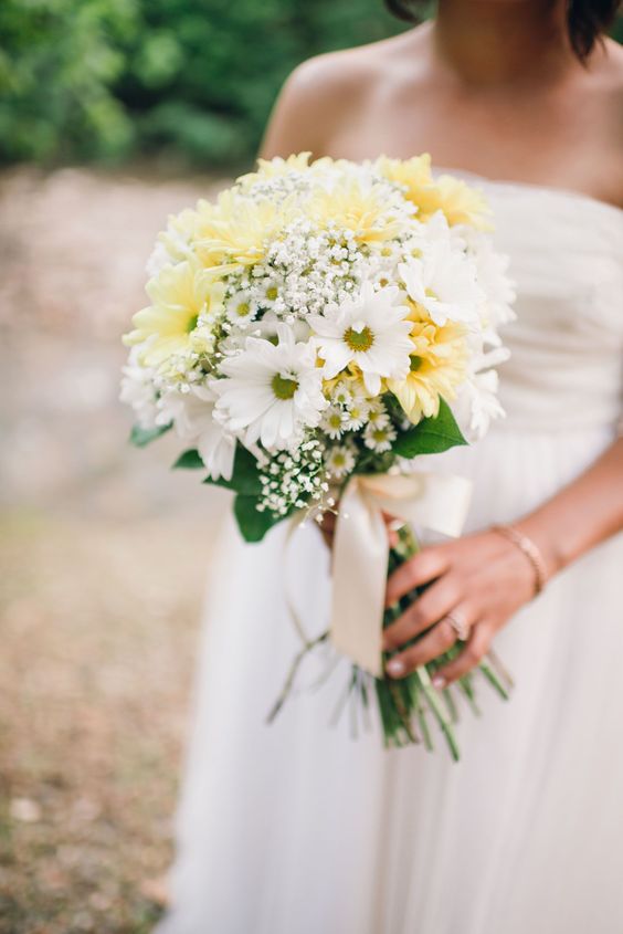 a beautiful wedding bouquet of white and yellow gerberas, baby's breath and greenery plus neutral ribbon for a spring or summer wedding