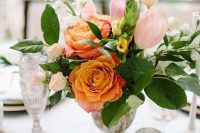 a beautiful wedding centerpiece of light pink tulips and roses, orange roses and greenery and candles around is wow