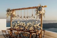 a beautiful wedding reception space with a sea view, with white and blue blooms on the table and over it, with bulbs hanging down