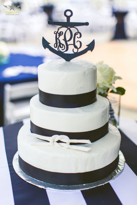 a black and white wedding cake with black ribbon, a rope knot and a black anchor with calligraphy on top is amazing