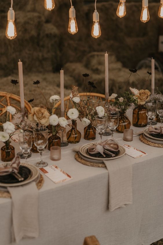 a boho wedding reception with blooms and dried grasses, with candles and bulbs over the table to increase coziness