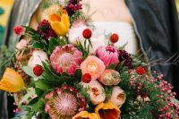 a bold and colorful wedding bouquet of orange tulips, pink king proteas and ranunculus, greenery and berries is a lovely idea for a bold wedding
