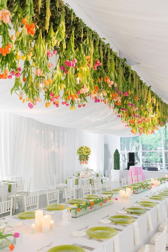 a bold and large overhead wedding installation of hanging pink, yellow, orange tulips and greenery and hanging candles is amazing