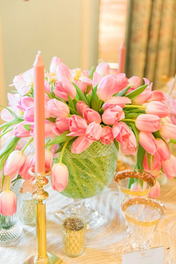 a bold and lush pink tulip wedding centerpiece in a crystal bowl, with pink candles and gold candleholders