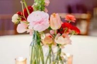 a bold cluster wedding centerpiece of clear vases with peachy and pink tulips and ranunculus and candles in small candleholders
