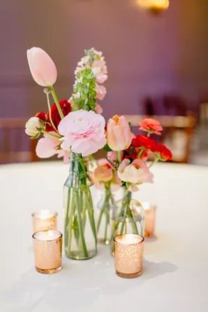 a bold cluster wedding centerpiece of clear vases with peachy and pink tulips and ranunculus and candles in small candleholders