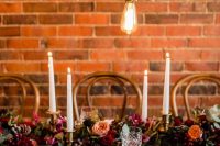 a bright wedding reception space with bold jewel-tone florals and greenery, elegant tall and thin candles, bulbs over the table for a chic look