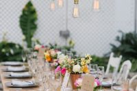 a bright wedding reception space with colorful blooms, greenery and bulbs over the table to make the space cozier and more welcoming