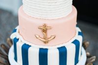 a catchy wedding cake with a white rope, pink and striped navy and white tier, a gold anchor is a chic and bold idea for a nautical wedding