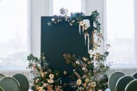 a chic and refined wedding backdrop of peachy and blue blooms, greenery, foliage, dried and fresh elements and a black canvas