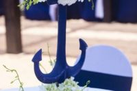a chic and refined wedding centerpiece of white blooms and greenery, a navy anchor and white blooms on it is a lovely idea for a nautical wedding