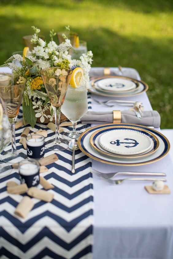 a chic nautical wedding tablescape with a chevron runner, navy, white and gold plates with anchor prints, candles, white blooms and greenery