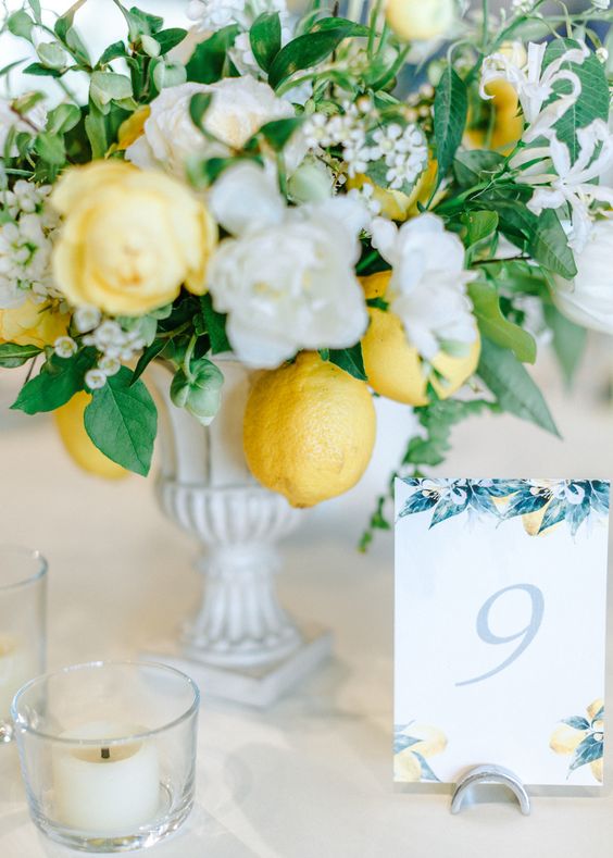 a chic vintage wedding centerpiece of a white urn with white and yellow blooms, greenery and lemons is awesome for summer