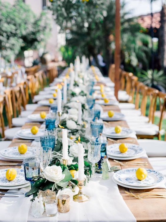 a chic wedding table setting with a neutral fabric runner, blue glasses, blue printed plates and lemons on the tables