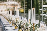 a chic wedding tablescape with a lush greenery and white bloom runner, tall and thin candles and lemons on the table