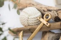 a coastal wedding centerpiece of driftwood, a gilded anchor, a rope ball and greenery is a cool and simple idea for a wedding
