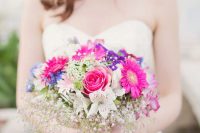 a colorful wedding bouquet of hot pink, purple, blue and neutral blooms and pink baby’s breath is amazing