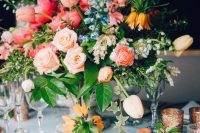 a colorful wedding centerpiece of peachy, pink and hot pink blooms including tulips, blue and white flowers, greenery is amazing