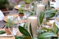 a cool wedding tablescape with a striped runner, a magnolia leaf and candle centerpiece and wicker chargers