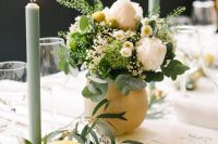 a creative summer wedding centerpiece of a large lemon as a vase for white and yellow blooms and greenery, a lemon and some greenery, olive green candles