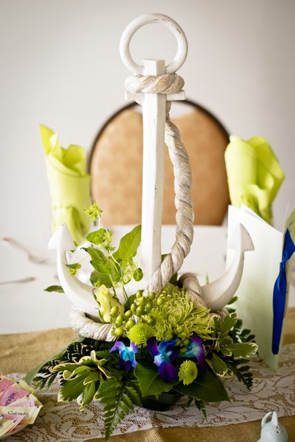 a creative wedding centerpiece of greenery, bold blooms, a white anchor and rope is a stunning idea for a bold tropical wedding