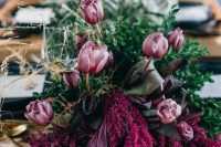 a dark and moody wedding centerpiece of purple tulips and fuchsia blooms, greenery and dark foliage makes a bold statement on a fall wedding table