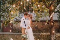 a delicate and touching wedding ceremony space with bulbs hanging down from the living tree and pillar candles around