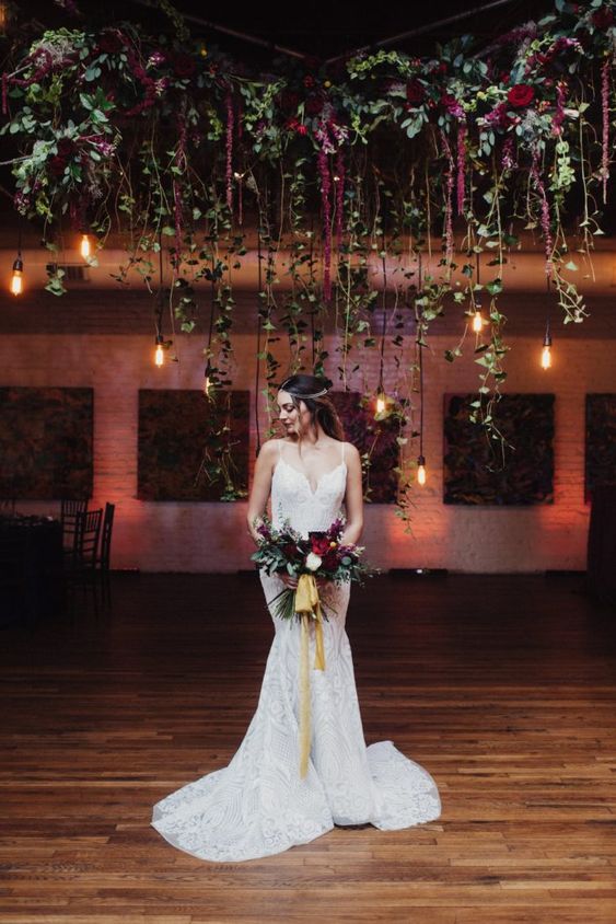 a fab wedding altar of greenery and burgundy blooms hanging down plus some bulbs is a very creative and cool idea