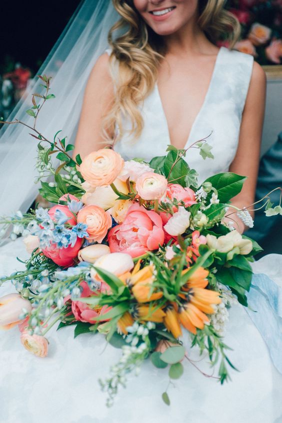 a fantastic wedding bouquet of peachy and orange blooms, pale pink tulips, yellow blooms and blue ones, greenery