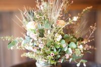 a farmhouse wedding centerpiece of a jar wrapped with twine, with greenery and waxflower is a lovely idea for a summer wedding