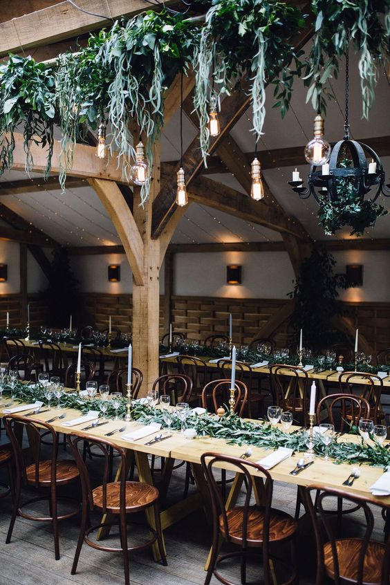 a fresh and inspiring wedding reception space with greenery on the table and greenery and bulbs over the table is amazing