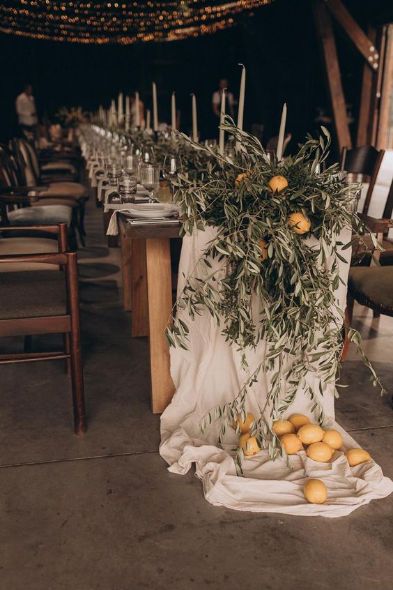 a gorgeous Italian wedding tablescape with white fabric, olive branches, tall and thin candles and lemons on the floor