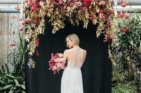 a gorgeous wedding backdrop of a black canvas, gilded foliage and leaves, pink, red, mauve and blush blooms and hanging flowers overhead